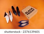 autumnal boots and flat shoes near shopping bag with black friday letters on orange, top view