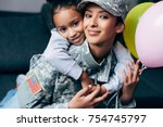 african american daughter hugging her mother in military uniform with balloons at home