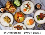 Small photo of Flat lay of a beautiful brunch selection with eggs on toast, burger, pork sandwich, waffle and chocolate, salad, espresso coffee and the daily newspaper