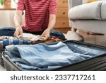 Preparing suitcase for summer vacation trip. Young woman checking accessories and stuff in luggage on the bed at home before travel.