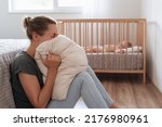 Small photo of Depressed mother screaming with anger and desperation in pillow to overcome negative emotions, suffering postnatal depression because of lack of help and support with childcare routine
