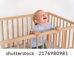 Portrait of upset sad frustrated one year old baby boy getting hysterical standing in bed asking to pick him up, seeking attention of parents crying out loud. Child temper tantrum