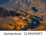 Small photo of Historic vintage biplane propeller with engine on fire and smoke before crash in dramatic sunset sky. Military reconnaissance aircraft of World war time