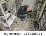 Small photo of A sad technician sits near a pile of wires and holds his head with his hands in an empty datacenter. The man is in a plundered server room.