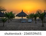Sunset above Atlantic Ocean and a beach with palm trees, sunshades and sunbeds in Senegal, Africa