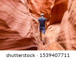 Orange red wave shape formations rocks shadows with back of man walking at narrow Antelope slot canyon in Arizona on footpath trail from Lake Powell
