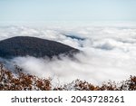 Clouds inversion fog at Devil's Knob Overlook at Wintergreen resort town in Blue Ridge parkway mountains with autumn fall foliage trees covering peak high angle view