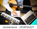 Small photo of top view of male songwriter writing a song with laptop computer and keyboard on desk. songwriting concept