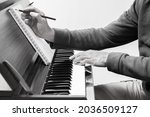Small photo of black and white male songwriter writing a song on music sheet while playing chord on acoustic piano keys. songwriting concept