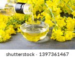 Pouring canola oil into the glass bowl against rapeseed blossoms on the grey surface, closeup shot