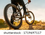 Man on mountain bike. Bicycle wheels close up image on sunset. Low angle view of cyclist riding mountain bike. Foot on pedal.