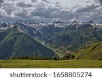 Small photo of View looking out over valley surrounded by snow capped mountains covered by gray clouded sky and bordered with yellow wild flowers in immediate foreground