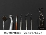 Small photo of Mouth mirror, a dental handpiece with bur, a brush, a curette, a plugger, a dental restoration instrument, a rubber dam clamp pliers with a clamp on the black background. Medical tools. Top view.