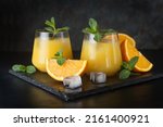 Refreshing summer drink with orange juice, mint and ice cubes in glasses on a wooden table