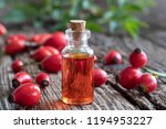 A bottle of rosehip seed oil with fresh berries on a rustic background
