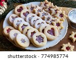 Linzer Christmas cookies filled with strawberry jam and dusted with sugar, arranged on a plate on a wooden table