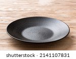 Perspective view of empty black plate on wooden background. Empty space for your design.