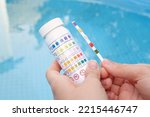 Small photo of Analysis of the PH and chlorine of the water in a swimming pool in Summer. Check quality of water with test strip, comparing results.