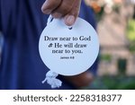 Small photo of Bible verse quote - Draw near to God and He will draw near to you. James 4:8 with person showing text on white circle label paper in hand. Christianity concept with bible verses quote.