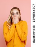 Small photo of Human emotion. Portrait of a young blonde girl posing in a yellow sweater on a pink background. The woman is frightened and covers her mouth with her hands. Expresses a strong fear and jitters.