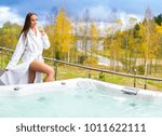 Small photo of Jacuzzi in the street. The girl takes a whirlpool bath. A girl in a bathrobe is standing by the hydromassage bath. whirlpool bath the balcony of the house. The jacuzzi is at the Cottage.