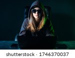 Woman hacker. Girl hacker works at a laptop in dark. Young hacker in a dark room. Hacking computer systems. Girl carries out a hacking attack. Young woman dangerous cybercriminal. Woman near computer