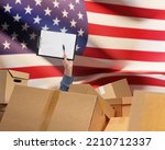 Delivery of goods to USA . Mans hand among cardboard boxes. Clipboard and USA flag. Concept of delivery by American regions. Hand of storekeeper among parcels. USA Delivery business. Copy space