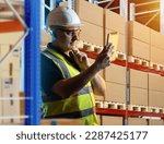 Small photo of Customs warehouse worker. Man with tablet computer. Guy near racks with boxes. Customs warehouse worker thought for moment. Man in reflective vest and safety helmet. Career in bonded warehouse