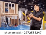 Small photo of Construction of exhibition pavilion. Man with phone in hands. Builders are preparing exhibition hall. Man stands in exhibition hangar. Construction of temporary wooden pavilions in hangar