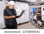 Small photo of Man is industrialist. Guy in production room. Engineer holding laptop. Man works in industrial enterprise. Engineer controls equipment via computer. Factory technologist in white hardhat