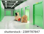 Small photo of Man rents storage unit. Warehouse with gates to containers for safekeeping. Cardboard boxes near storage unit. Guy with phone in hallway of warehouse building. Storage unit inside building.