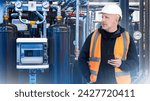 Small photo of Man industrial worker. Engineer near gas equipment. Man with phone stands inside factory. Gas boiler room maintenance engineer. Industrialist guy writes SMS. Industrial tech implementation specialist