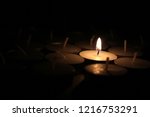 Small photo of Typical aluminium burning tea candle isolated on white background with shadow reflection. Tea candle with flame and black wick. Tea candle with burning ingle and burned candlewick. Macro photography