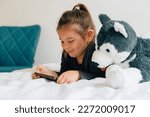 preschool age girl watching cartoons on smartphone on bed. Plush toy dog