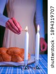 Small photo of Shabbat traditions in rabbinical Judaism: Jewish woman lighting Sabbath candles on Friday evening, with traditional challah bread in the background