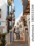 Small photo of A view of a narrow street in the amiable, pretty small white village of Peniscola, in Spain. A picturesque narrow winding street with brightly painted pots with fresh flowers.
