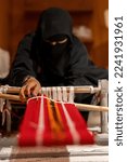 Small photo of Doha, Qatar - December 14, 2022: a diligent woman in Abaya makes a colorful traditional woolen carpet by hand, a pile rug, Selective Focus