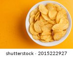 Potato chips in bowl on yellow background, top view. Unhealthy food, rich in saturated fatty acids
