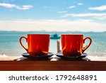 Red coffee cup couple on the balcony in the morning with sunshine and sea view background. Hot coffee after wake up for refreshment in the morning. Coffee time, summer vacation in the concept.