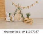 Small photo of Interior design of easter living room with easter bunny sculptures, garland, plants, wooden boxes,flags garland, tent, wigwam. Home decor.Warm and cozy composition