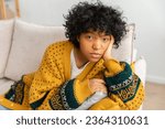 African american sad thoughtful pensive unmotivated girl sitting on sofa at home indoor. Young african woman ponder look tired after long day. Girl feels depressed offended lonely upset heartbreak