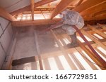 Worker with a hose is spraying ecowool insulation in the attic of a house. Insulation of the attic or floor in the house