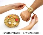 Close up top view of female  hands tying colorful rakhi on her brother’s hand with brass dish full of puja accessories in selective focus against  white background on Raksha Bandhan Festival 