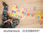 Small photo of Two year boy playing with wooden alphabet letters board on the floor. Intellectual game, preschool implement for early education. Verbal and memory training exercise.