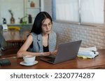Small photo of Close-up Asian woman typing on laptop computer, was busy, gave dazed look before looking at computer screen and reaching over open document lying on table, turn around type work on computer again.