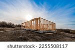Small photo of The structure of wood framing at construction site against a vast cloudy sky with bright sun behind. New build home at empty lot. framework ready for wall and roof install. Real estate development.