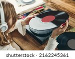 Small photo of Young woman listening to music from vinyl record player. Playing music on turntable player. Female enjoying music from old record collection at home. Stack of analog vinyl records. Retro and vintage
