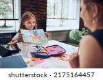 Girl presenting her artwork teacher. Woman assisting schoolgirl during classes at primary school. Child drawing picture sitting at desk in classroom. Girl drawing pictures. Learning at primary school
