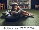 Schoolgirl reading book in school library. Primary school pupil is involved in book. Child doing homework. Smart girl learning from book. Benefits of everyday reading. Child curiosity