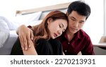 Small photo of Loving Asian man trying reconcile with his wife after quarrel. Guy embracing his crying suppose while sitting at their bed room